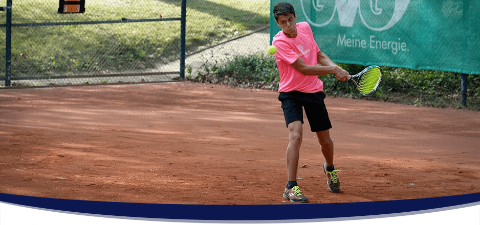 Männlicher Tennisspieler schlägt eine Rückhand auf einem Aschenplatz