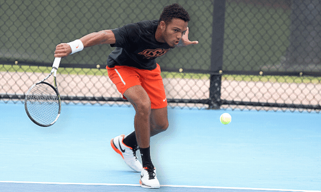 Male tennis player from oklahoma state university is hitting a slice backhand.