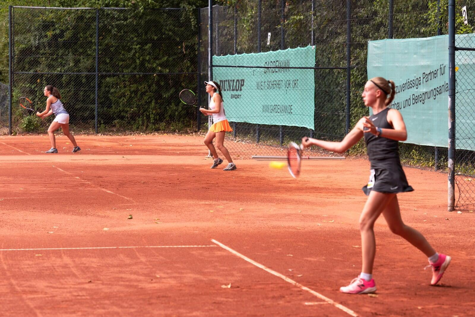 three female tennis players on three clay courts