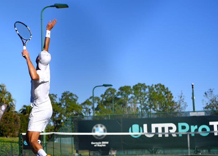 Lefty male tennis player with an all white outfit is serving
