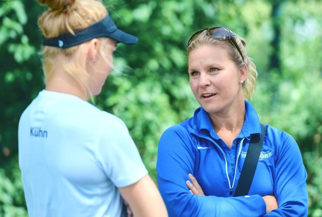 female college coach in a blue jacket talking to a female tennis player in a white shirt